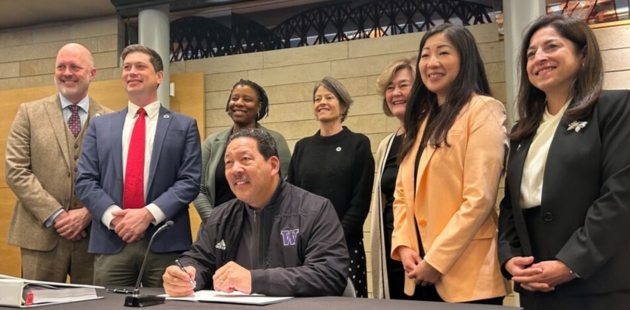 Photo of council members standing behind Mayor Bruce Harrell as he holds a pen over a document
