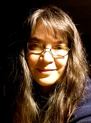 Tammie Dupuis has long brown hair, bangs, and wears glasses.