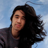 An Asian nonbinary person with their long black hair blowing in the wind