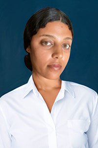 Zabia's black hair is pulled back tightly across her head and she wears a white button-up shirt.