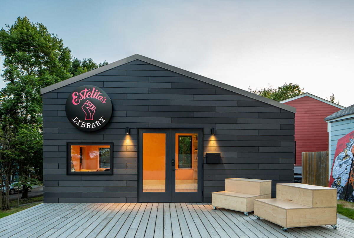 A small building structure with the business name "Estelita's Library" on the front of it. There are two large benches on the right.