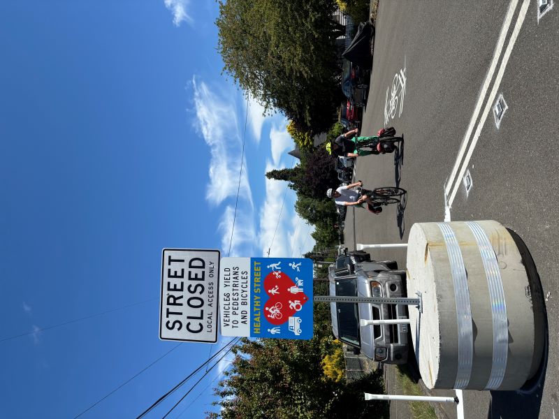 Healthy Street sign with people biking in the street.