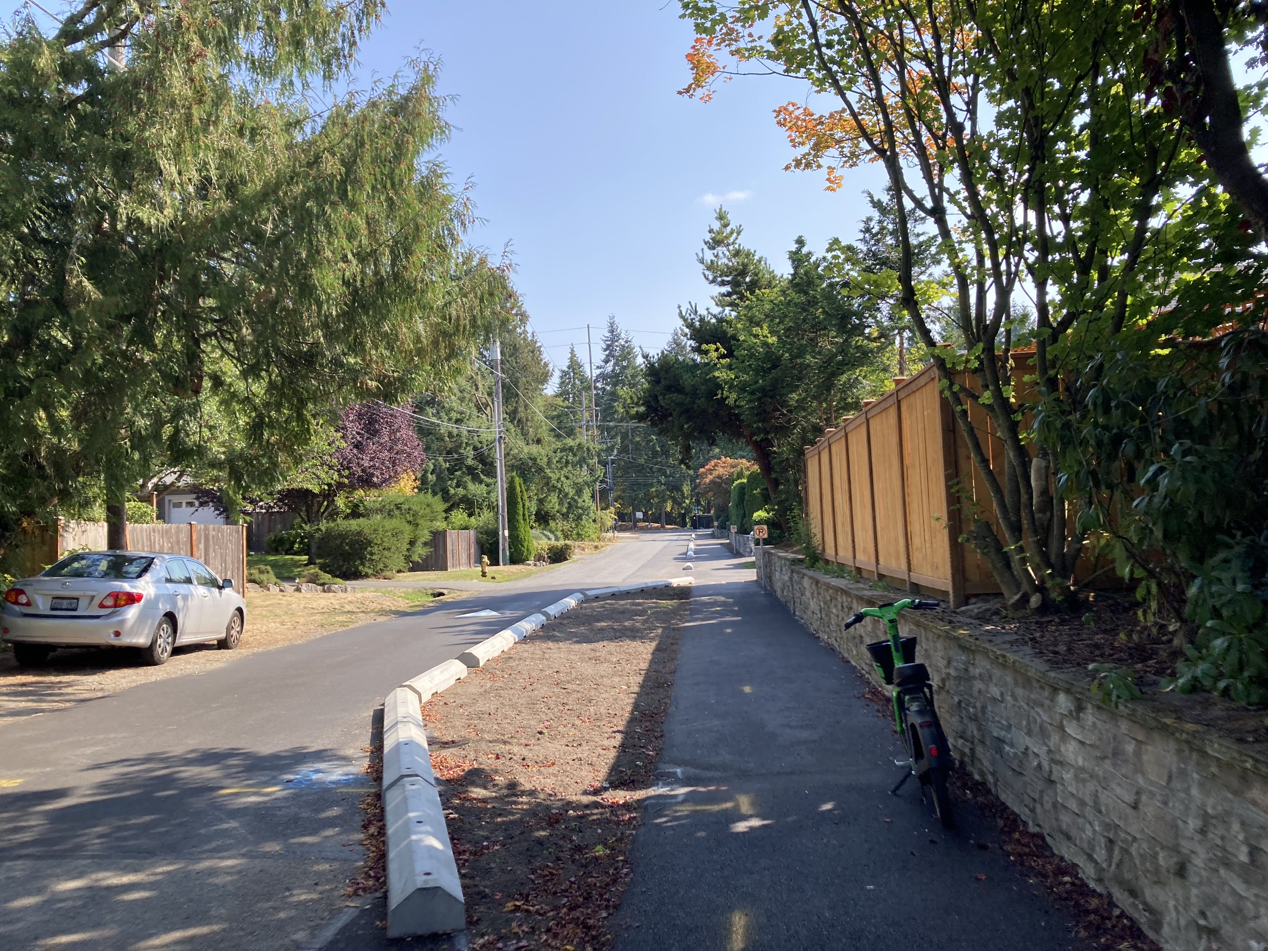 Asphalt walkway protected by asphalt wheel stops and chicane reducing width of traffic lane.