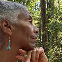 Rita is looking in profile in a forest, she's wearing turquoise earrings