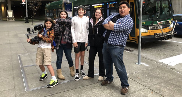 A group of five young people who participated in the Youth Ambassador program.  They are out on a city sidewalk, with a bus behind them. 
