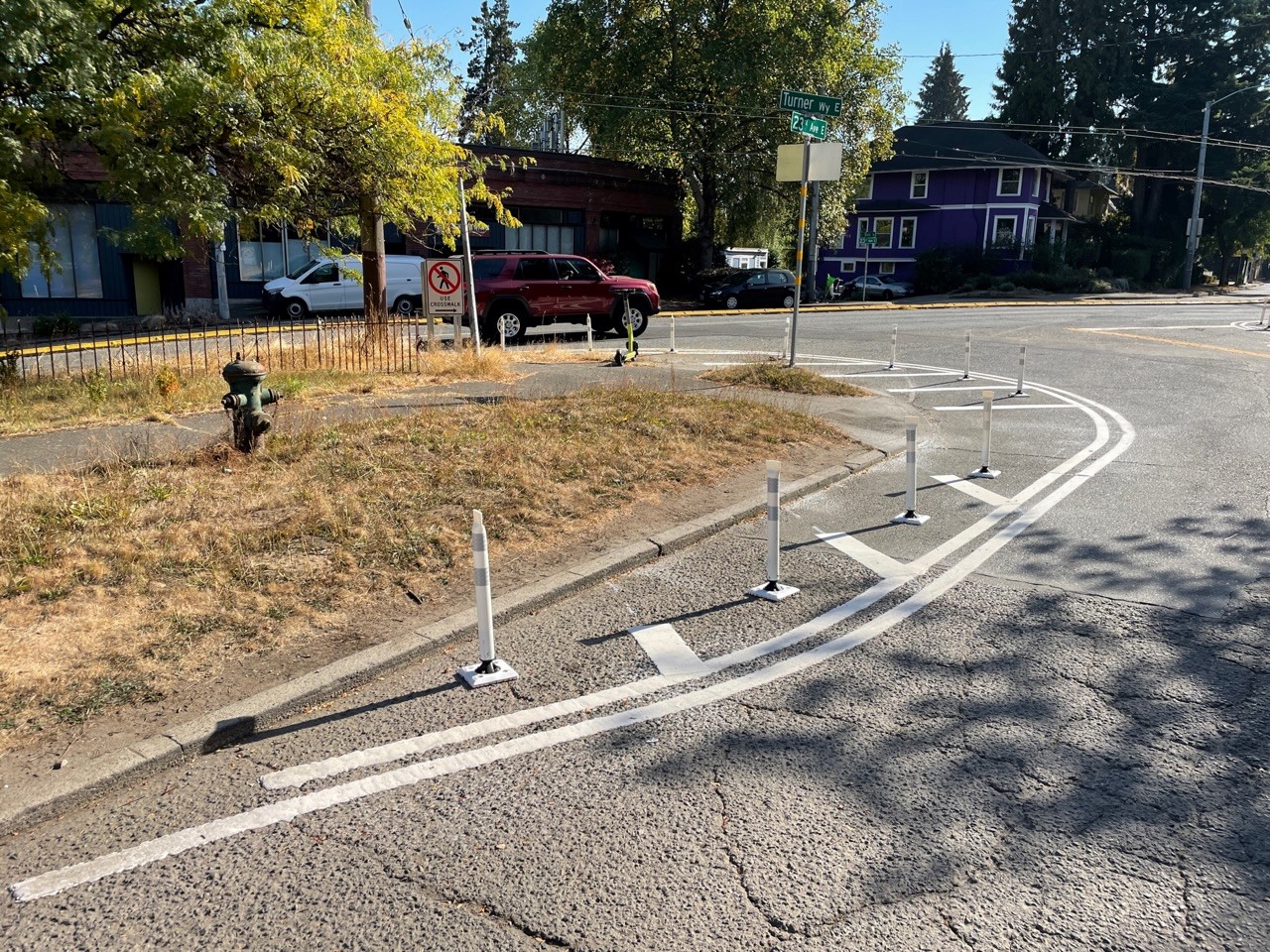 A picture showing a street with curved white lines painted and white posts in the street.
