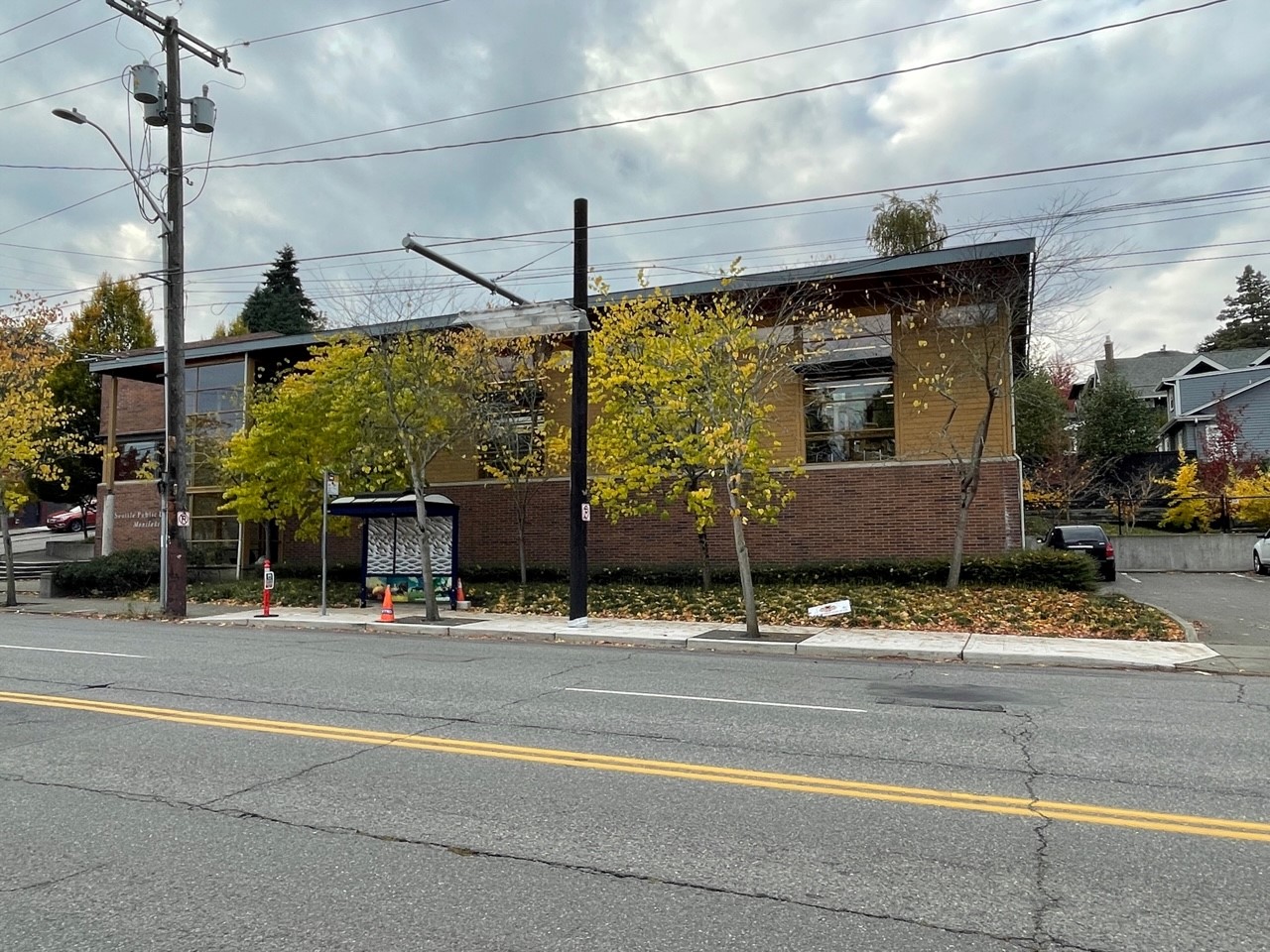 A picture of a building with a bus stop and bus shelter in front of it. 