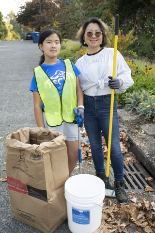  person squats next to a drain, sweeping dirt and debris into a dustpan.