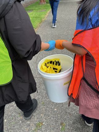 Two people carry a bucker of supplies together.