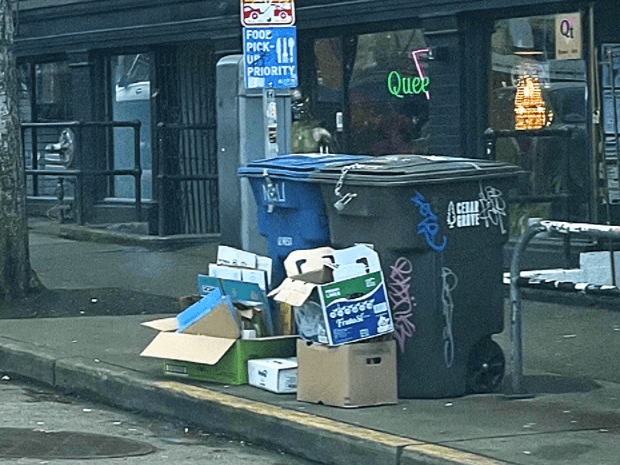 Cardboard piled up around bins on sidewalk.