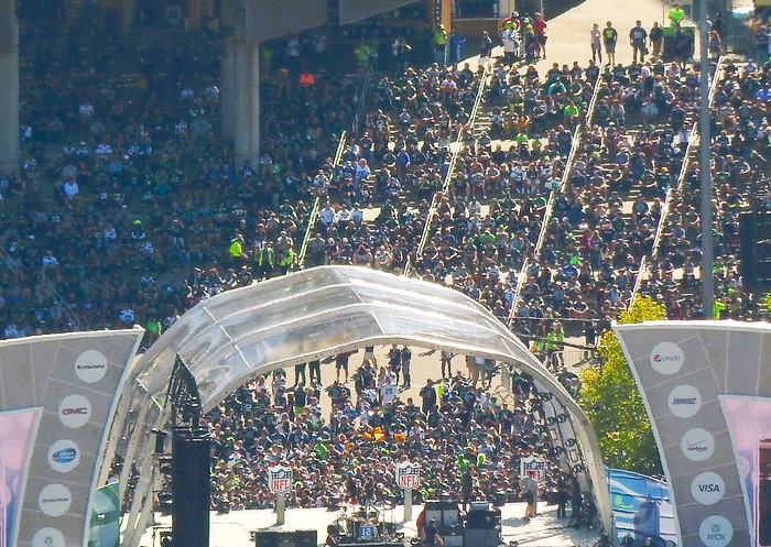 An aerial view of a large crowd gathered in front of a stage outside the entrance to Lumen Field