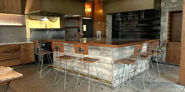 ከበስተጀርባ ጠረጴዛዎች እና ኩሽና ያለው ባር ያለው ባዶ ምግብ ቤት 