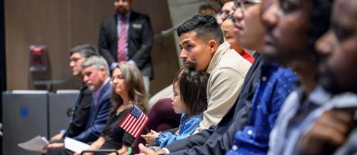 Man in auditorium holding young daughter on his lap while she waves a small American flag.