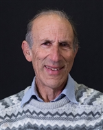 Andrew smiling at the camera in a patterned sweater in front of a dark background