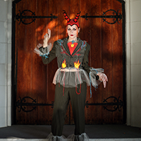 Model Ely wearing a suit embroidered with flames and spider webs and a hat with devil horns.