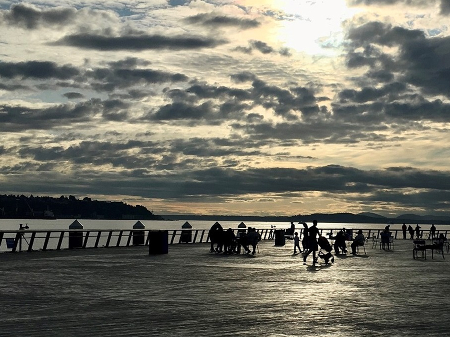 people strolling and sitting on the new Pier 62 looking toward Elliott Bay at sunset