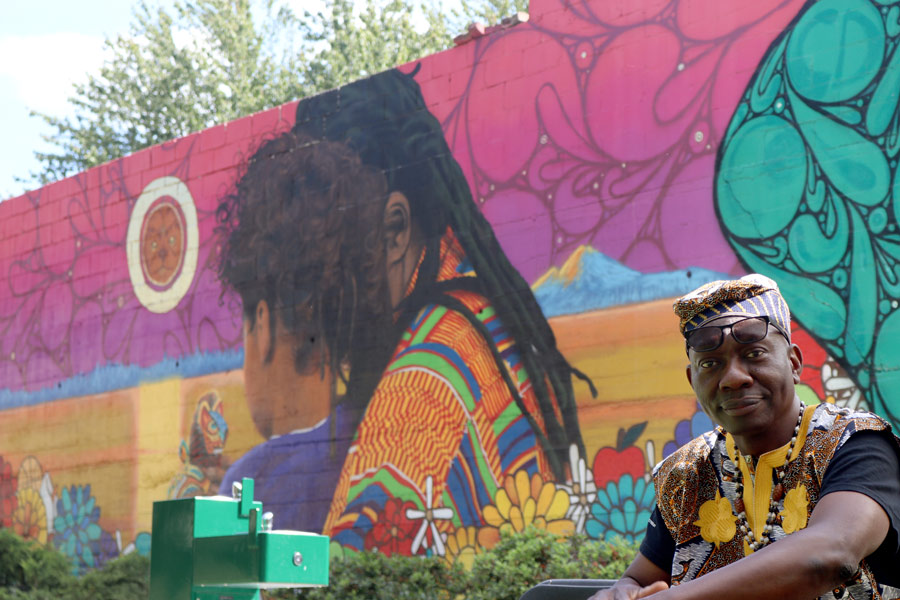 Spruce Street Mini Park Mural - Man in front of mural painting of a father and son with flowers and spirit animal