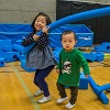 Two young children play with foam tubes in an indoor gym.