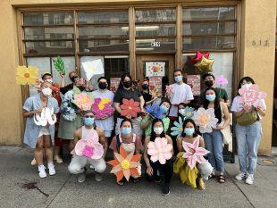 A group of people wearing masks posing for a photo holding colorful artwork