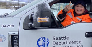 An SDOT employee giving a peace sign inside of a truck covered with snow
