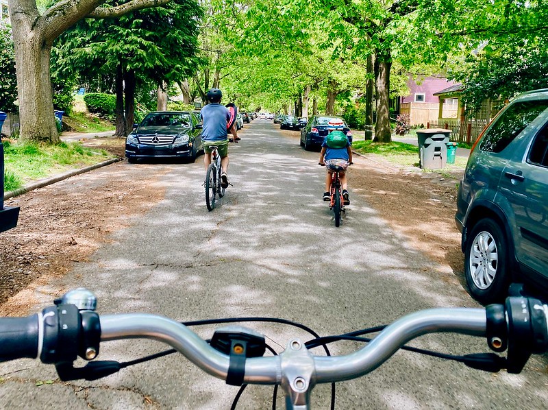 Someone takes a photo over the handlebars of their bike, capturing two riders ahead of them on an Healthy Street