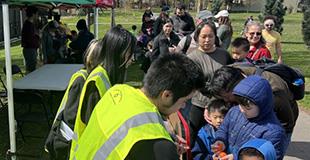 A line of people at a park leads to an activity table