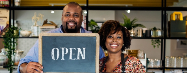 Two bakery owners smiling while holding an open sign.