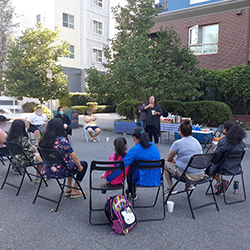 A community get together where peole are sitting around while someone is standing up speaking