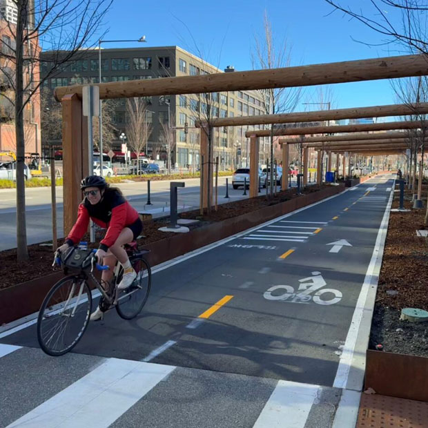 A biker on the path underneath Oscar Tuazon’s "To Our Teachers deqʷaled (Houseposts)", one of the new permanent artworks on the waterfront.